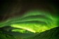 A view of the northern lights through a snow-covered mountain valley.